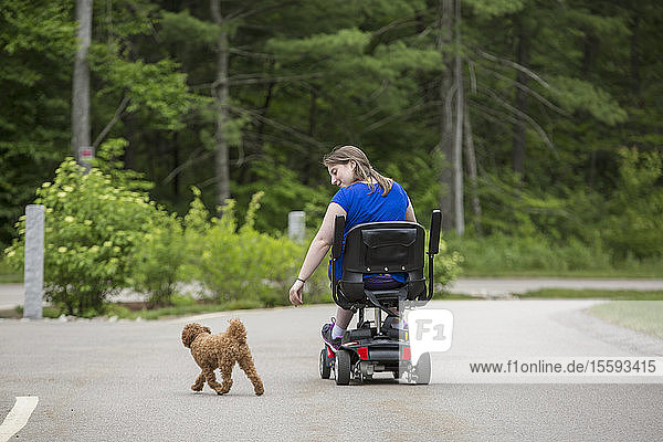 Junge Frau mit zerebraler Lähmung spielt mit ihrem Hund  während sie auf ihrem Roller sitzt