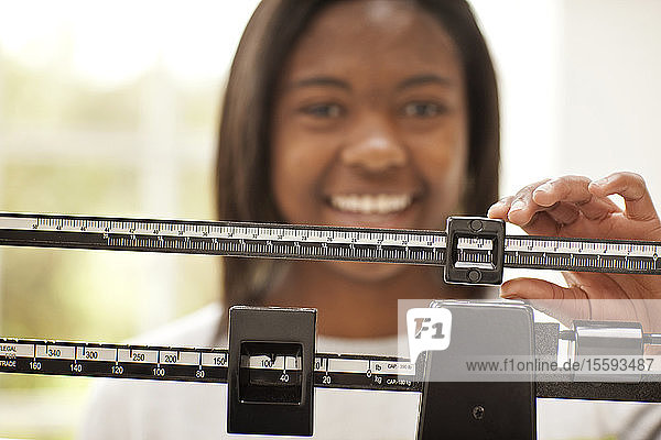 Smiling teenage girl adjusting the slide on a medical weight scale.