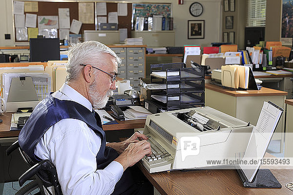 Mann mit Muskeldystrophie im Rollstuhl bei der Arbeit in einem Büro
