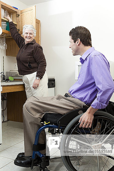 Home health aid getting a glass for a man in wheelchair with spinal cord injury