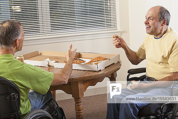 Two disabled men sitting in wheelchairs and eating pizza