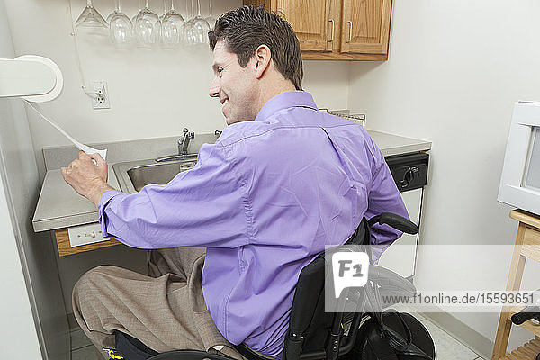 Mann im Rollstuhl mit Rückenmarksverletzung benutzt einen Papierhandtuchhalter in einer barrierefreien Küche