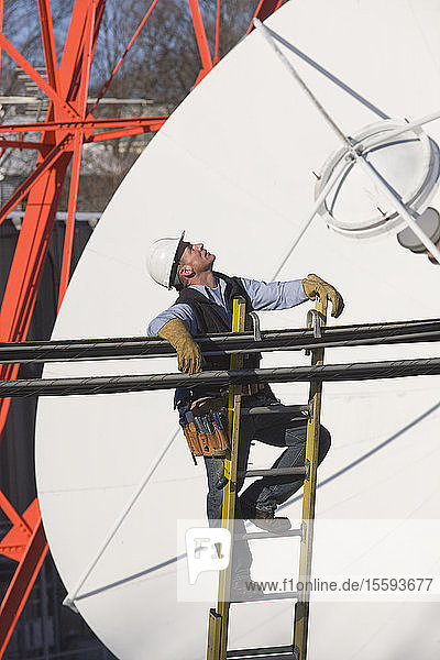 Kabelmonteur klettert auf eine Leiter  um eine Übertragungsleitung zu reparieren