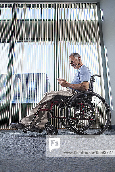 Mann mit Rückenmarksverletzung im Rollstuhl telefoniert in einem Bürokorridor