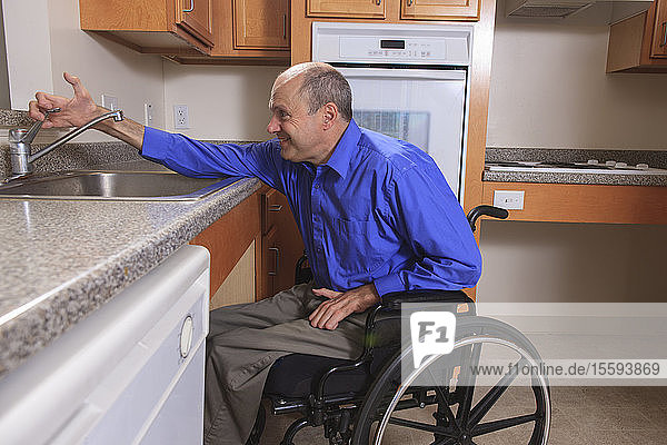 Mann mit Friedreich-Ataxie und deformierten Händen benutzt seinen Wasserhahn in der Küche