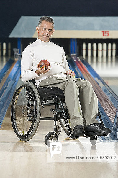 Portrait of a mature man with a Spinal Cord Injury holding a bowling ball and smiling