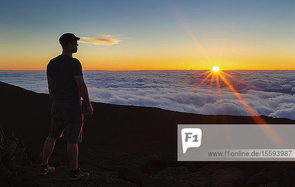 Silhouettierter Mann steht auf einem Felsen über den Wolken bei Sonnenuntergang  Haleakala; Maui  Hawaii  Vereinigte Staaten von Amerika