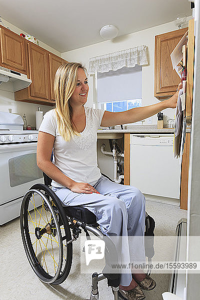 Frau mit Querschnittslähmung in ihrer barrierefreien Küche  die auf eine Hinweistafel schaut