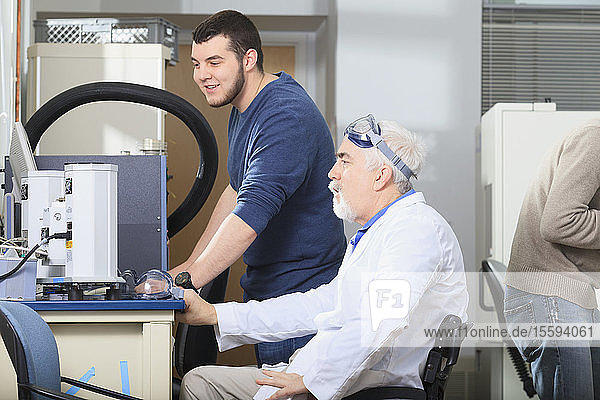 Professor with muscular dystrophy working on thermal gradient analyzer with engineering student in a laboratory