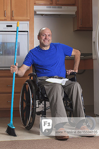 Mann mit Friedreich-Ataxie und deformierten Händen reinigt sein Haus vom Rollstuhl aus mit einem Besen