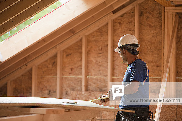 Ein spanischer Zimmermann misst ein Stück Ummantelung an einem im Bau befindlichen Haus aus