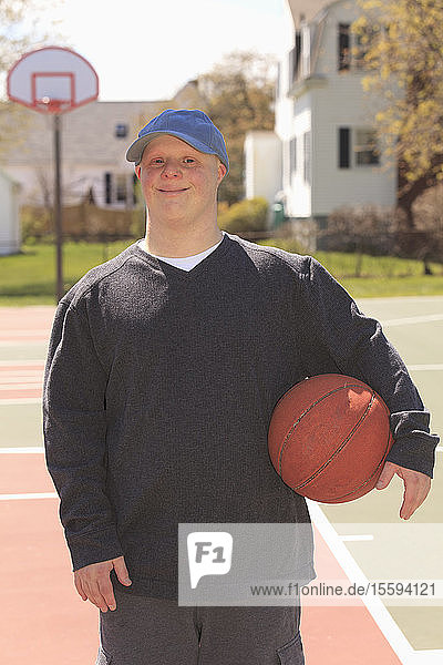 Porträt eines jungen Mannes mit Down-Syndrom  der im Park einen Basketball hält