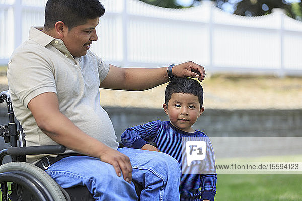 Hispanischer Mann mit Rückenmarksverletzung im Rollstuhl mit seinem Sohn auf dem Rasen