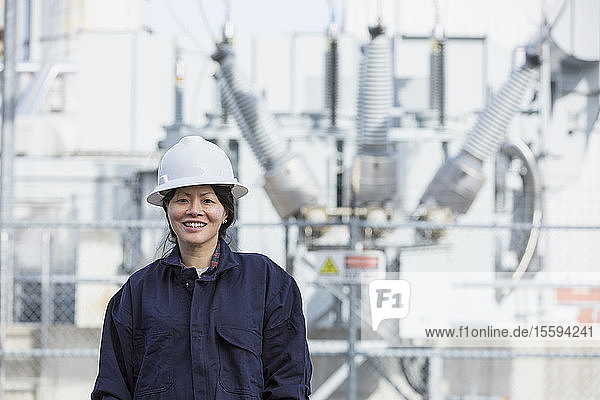 Porträt einer Energietechnikerin vor einem Hochspannungstransformator in einem Kraftwerk