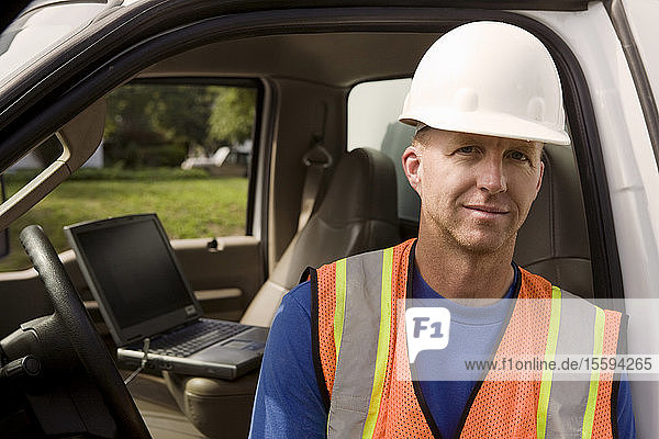 Porträt eines Bauarbeiters  offener Lastwagen mit Laptop im Hintergrund