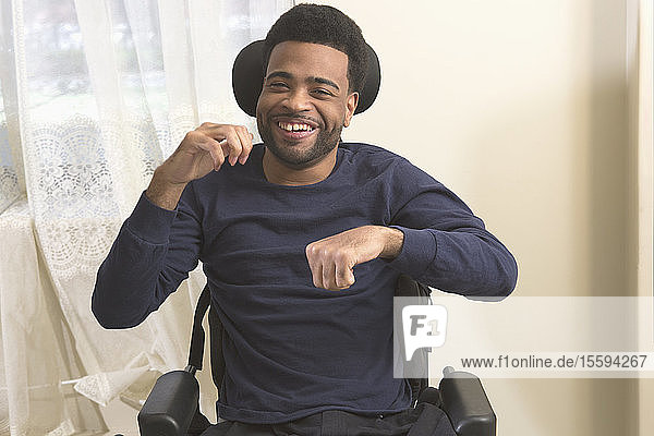 Glücklicher afroamerikanischer Mann mit zerebraler Lähmung lächelt zu Hause im Rollstuhl