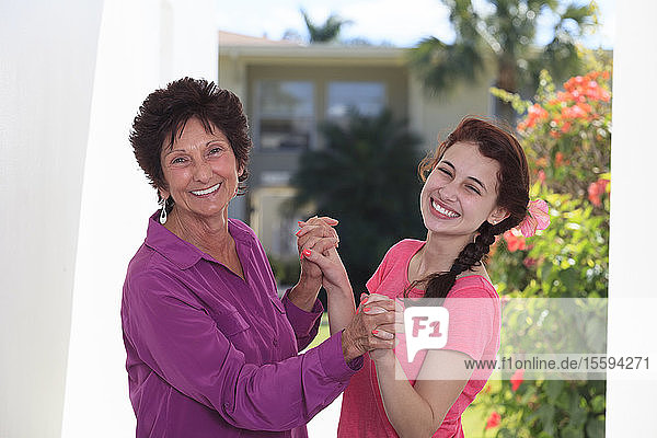 Lächelnde ältere Frau und ihre Enkelin  die sich gegenseitig die Hände halten