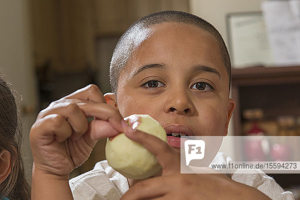 Porträt eines hispanischen Jungen mit Autismus  der einen Apfel isst