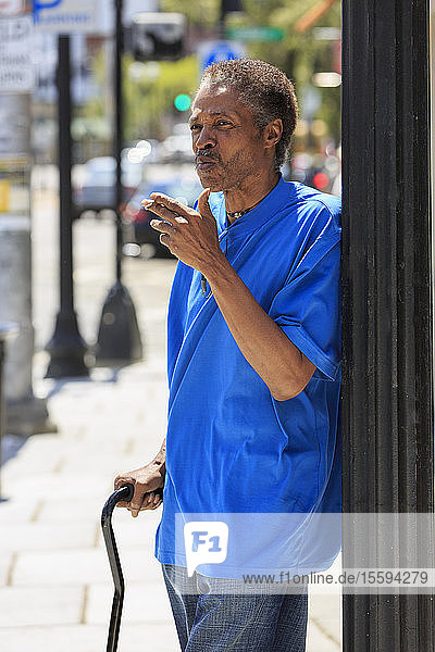 Mann mit traumatischer Hirnverletzung mit Stock raucht auf der Straße