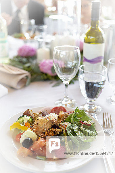 Formal table at a wedding with plate full of food and wine bottle with wine glasses; British Columbia  Canada