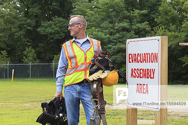 Communications engineer with climbing equipment and tool belts at evacuation assembly area