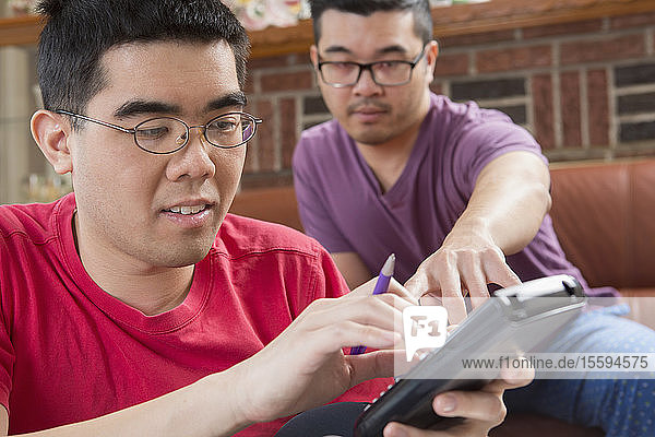 Asiatischer Mann mit Autismus arbeitet mit seinem Bruder am Telefon an seinen Hausaufgaben