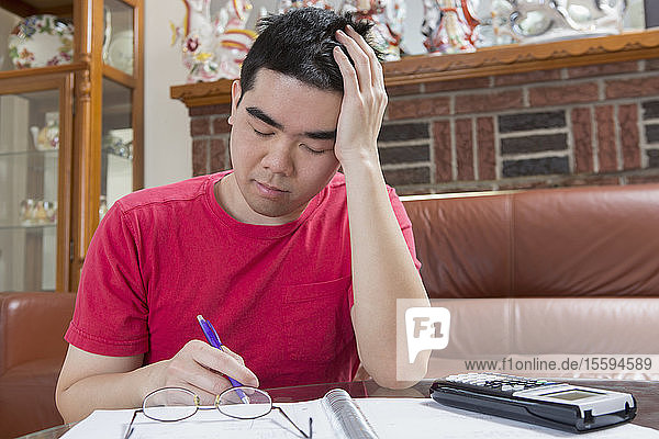 Asiatischer Mann mit Autismus arbeitet an seinen Hausaufgaben und wird müde