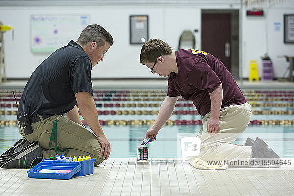 Junger Mann mit Down-Syndrom arbeitet an einer Hochschule und testet mit seinem Betreuer den PH-Wert im Schwimmbad