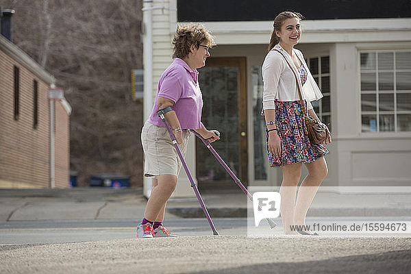 Frau mit Cerebralparese und Krücken geht mit ihrer Schwester in der Stadt spazieren