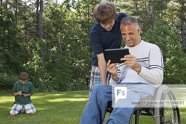 Man with spinal cord injury in wheelchair with his sons reading a tablet