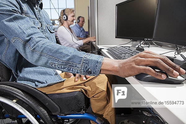 Mann mit Spinaler Meningitis im Rollstuhl bei der Arbeit an einem Stand in einem Callcenter