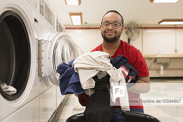 Glücklicher afroamerikanischer Mann mit Down-Syndrom beim Wäschewaschen im Hauswirtschaftsraum