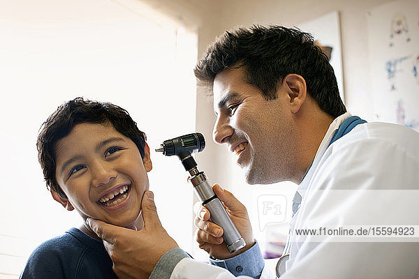 Ein Arzt untersucht das Ohr seines jungen Patienten mit einem Otoskop.