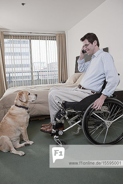 Ein Mann im Rollstuhl mit einer Rückenmarksverletzung spricht mit einem Diensthund über ein Mobiltelefon