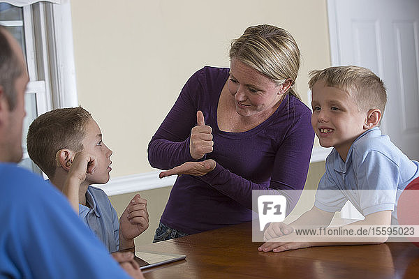 Mother and son communicating in American Sign Language about 'Hearing aid and help' at home