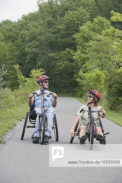 Ein junger Mann mit einer Rückenmarksverletzung und eine junge Frau fahren mit adaptiven Fahrrädern