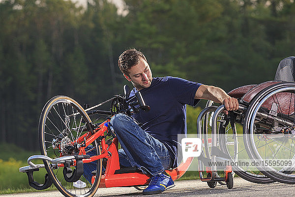 Ein Mann mit einer Rückenmarksverletzung in seinem speziell angefertigten adaptiven Handbike beim Einsteigen in seinen Rollstuhl