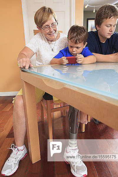 Grandmother with a prosthetic leg looking at a cell phone with her grandsons