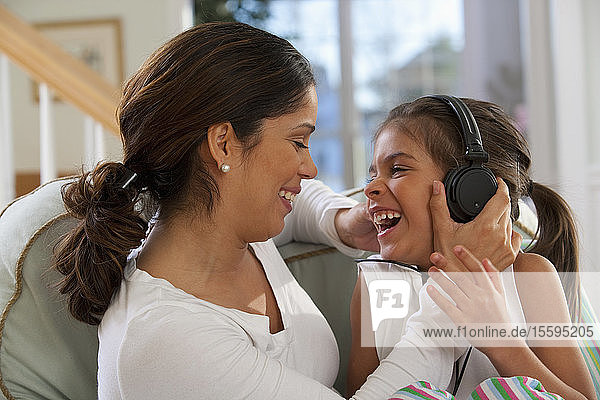 Hispanic girl sitting with her mother and listening to music