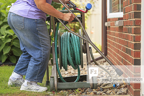 Frau mit Spina Bifida geht an Krücken und zieht einen Gartenschlauch
