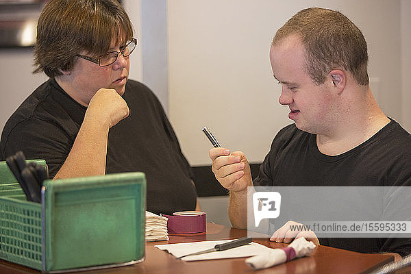 Waiter with Down Syndrome preparing napkin and silver with another colleague in a restaurant