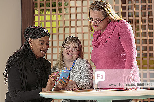 Drei Frauen in einem Büro lesen Textnachrichten  eine davon mit Down-Syndrom