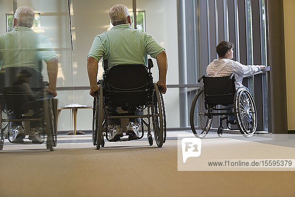 Älterer Mann mit Muskeldystrophie und eine junge Frau sitzen im Rollstuhl in einer Bibliothek