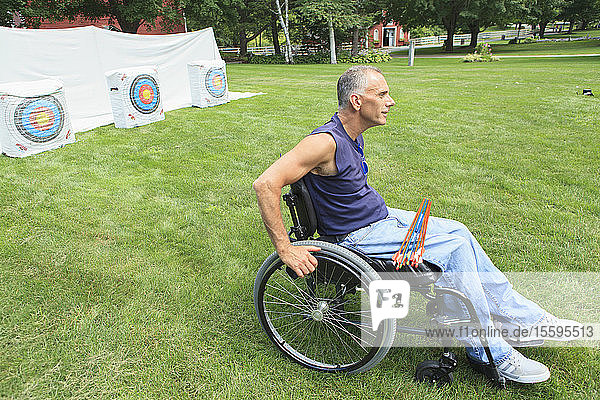 Mann mit Querschnittslähmung im Rollstuhl bereitet sich auf Bogenschießen vor