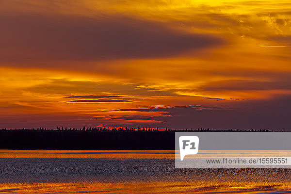 Dramatischer glühender Himmel bei Sonnenuntergang über einem See und einer silhouettierten Uferlinie; Saskatchewan  Kanada