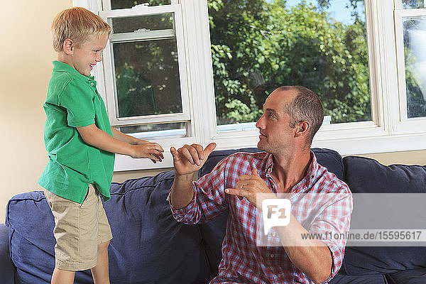 Father and son with hearing impairments signing 'play' in American sign language on their couch