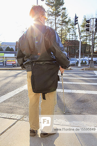 Mann mit angeborener Blindheit  der mit seinem Stock die Straße überquert
