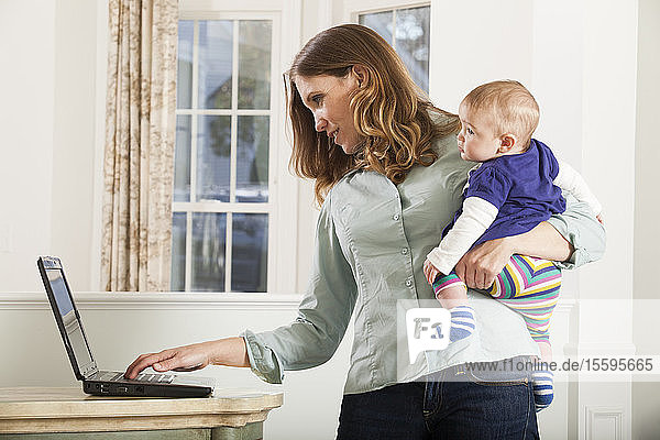 Woman working on a computer at home while holding baby