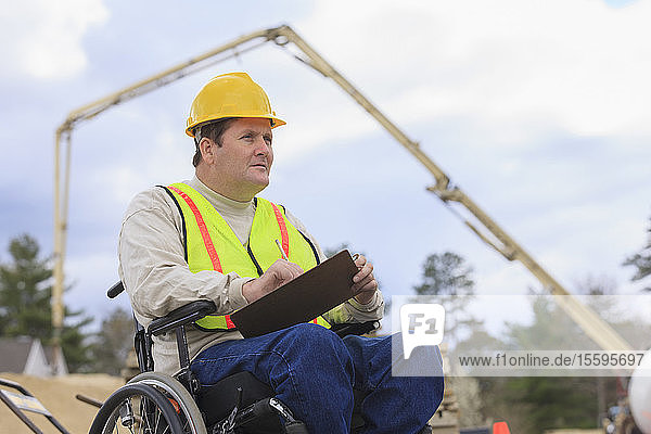 Construction supervisor with Spinal Cord Injury taking notes with concrete pump in background
