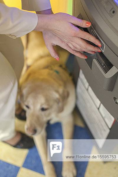 Junge blinde Frau  die mit ihrem Diensthund an einem Bankautomaten wartet